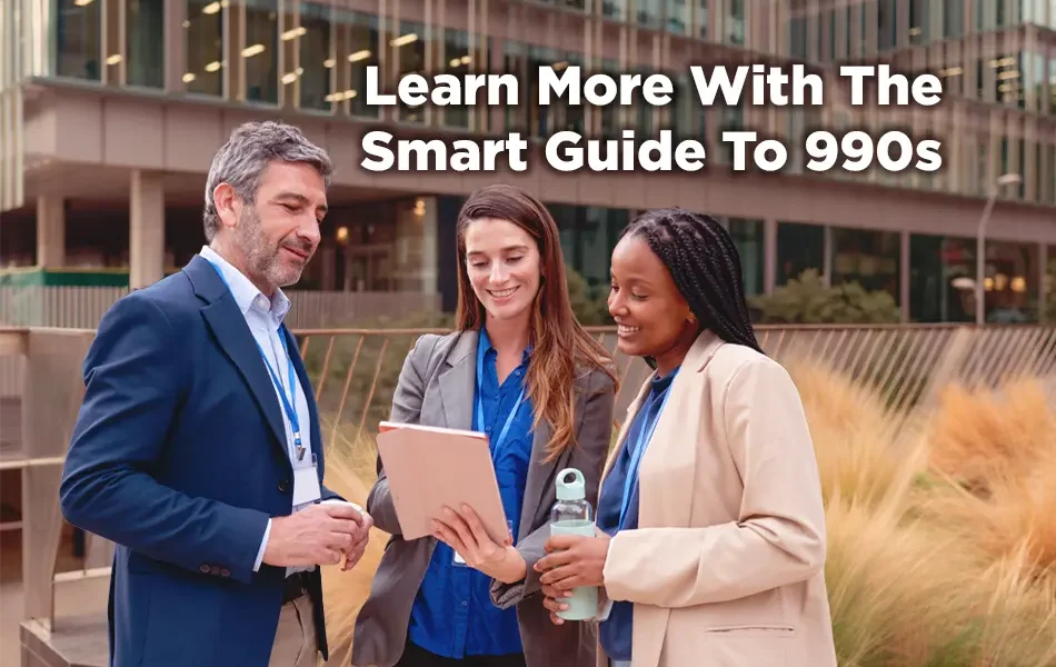 Three nonprofit professionals stand outside a modern office building, smiling and reviewing a tablet together, with on-image text reading “Learn More With The Smart Guide To 990s.”