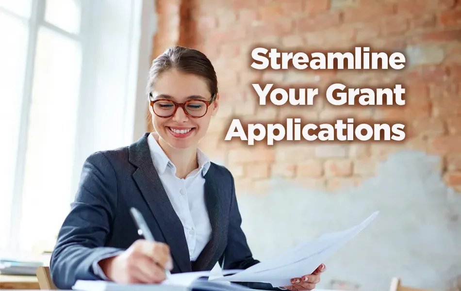 A grant writer sits at her desk writing a grant she knows has an excellent chance of winning. She's smiling as she works. The caption reads: Streamline Your Grant Application.
